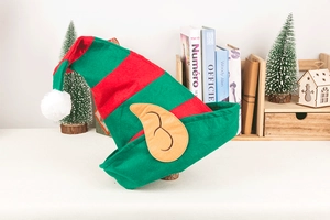 Detail of a red and green striped Christmas elf hat with yellow ears on a festive table
