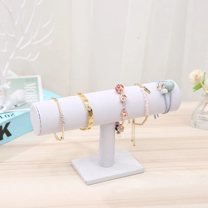 Close-up of a white T-bar jewelry stand displaying gold bracelets and pink bead charms