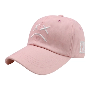 Pink cotton baseball cap with white sad face embroidery and curved brim on white background