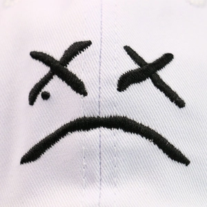 White cotton baseball cap with black embroidered sad face emoji and detailed stitching