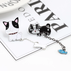 Asymmetric enamel earrings with cute dog and cat pendants on a magazine background