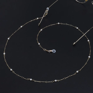 Catenina per occhiali fatta a mano in rame dorato con perle bianche su sfondo scuro