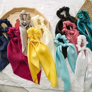 Multiple colors of satin silk hair scrunchies with long ribbons on white textured background