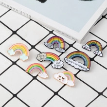 Detail view of colorful rainbow and cloud enamel pins on a checkered background with a magazine
