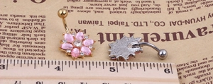 Close-up of flower belly button rings in gold and silver with pink rhinestones and ruler