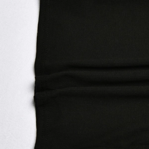 Macro shot of black ribbed knit fabric showing the detailed texture and hem finish of the dress
