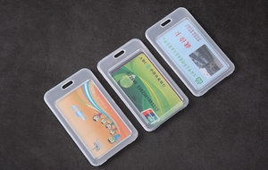 Three transparent rigid plastic card holders with lanyard holes on a textured surface