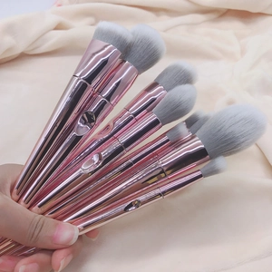 Close-up of 10 rose gold makeup brushes with grey-white fibers held against beige fabric