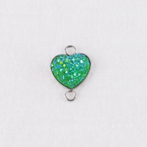 Macro detail of a 13mm green heart charm connector with shimmering crystals in metal base