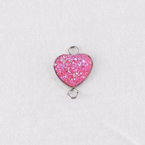 Close-up of heart-shaped pink glitter resin connector with silver metal frame for DIY