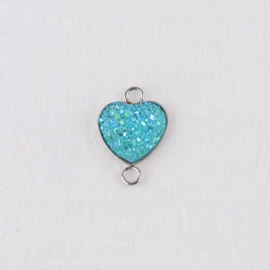 Macro detail of a 13mm heart-shaped pendant with teal glitter resin and silver-tone frame
