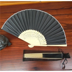 Macro view of a black folding fan with light wood ribs and a matching mesh storage bag