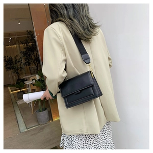 Side view of a black leather crossbody bag with wide strap on a model in a beige blazer