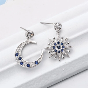 Asymmetric silver moon and star earrings with blue zircon stones on white texture