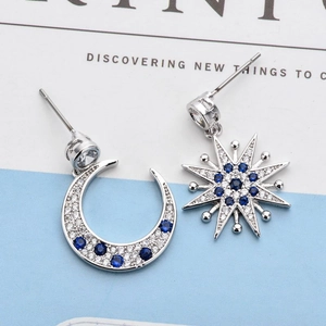 Detailed macro view of asymmetric star and moon earrings with blue and white zircon