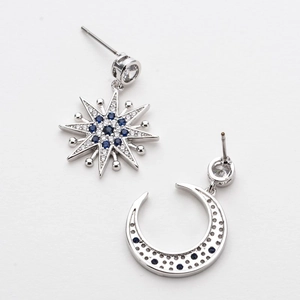 Detail of silver asymmetric earrings with moon and star motifs and blue cubic zirconia