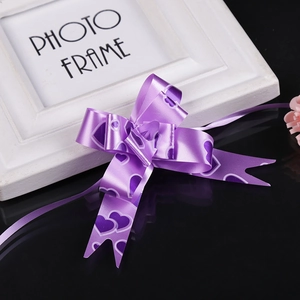 Close-up of purple heart pattern ribbon pull bow on reflective black surface with decor