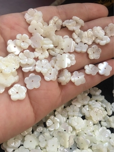 Close-up of 10mm white carved shell flower beads for DIY jewelry making in palm