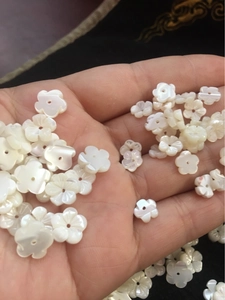 Detailed view of hand holding carved white shell flower beads with iridescent luster