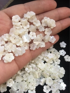 Close-up of white carved shell flower beads for DIY jewelry making held in palm