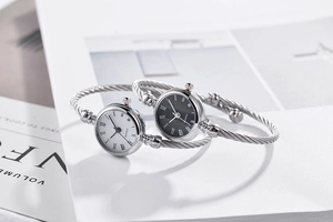 Silver twisted bangle quartz watches with Roman numeral dials displayed on an open magazine