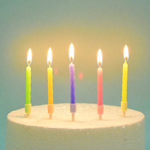 Close-up of five colorful spiral birthday candles lit with plastic holders on cake