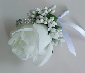 Detail of white artificial rose boutonniere with green leaves, berries and ribbon