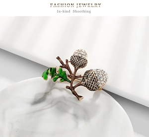 Detail of acorn brooch showing green enamel leaf and crystal rhinestones on marble