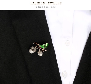 Detail of hazelnut brooch with sparkling rhinestones and green enamel leaf on black suit