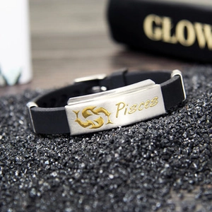 Detail of black silicone bracelet featuring a metal plate with gold Pisces zodiac engraving