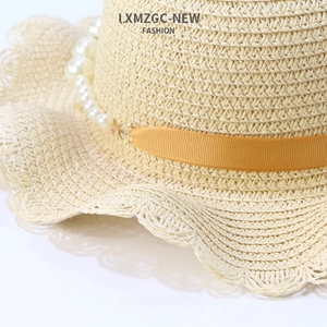 Detailed view of the wavy brim weave and white pearl string on an ivory straw sun hat