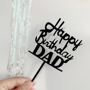 Detail shot of black acrylic Happy Birthday DAD cake topper held by hand