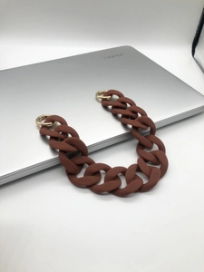 Close-up of matte brown resin chain strap with gold metal rings on a laptop corner