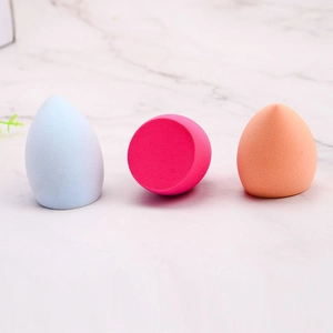 Three colorful makeup sponges in blue, pink, and orange on a white marble surface