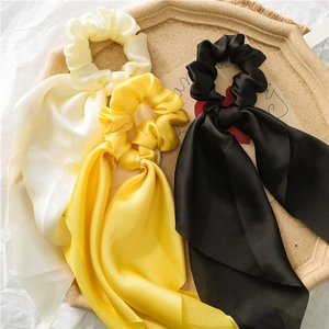 Close-up of three satin bow hair ties in white, yellow, and black on a stone tray
