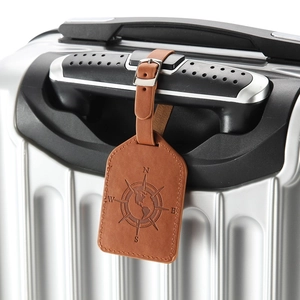 Brown PU leather luggage tag with embossed compass design hanging on a silver suitcase