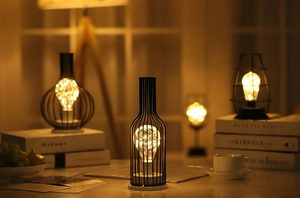 Close-up of wire LED lights inside black iron wine bottle and glass frames on a table