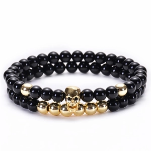 Dettaglio di bracciali elastici con perline di onice nero e teschi metallici dorati
