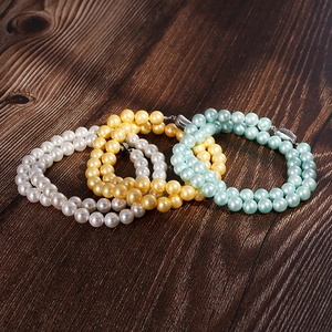Classic 8mm round pearl bracelets in white, yellow and blue on a wood surface