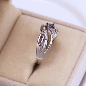 Macro shot of silver ring with teal center stone and pink heart-shaped accents