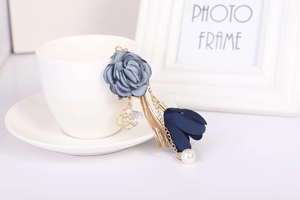 Dettaglio portachiavi fiore in tessuto blu con nappe dorate e perle su tazza bianca