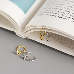 Detail of silver and gold Evil Eye earrings with blue gemstones clipped on book pages