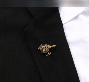 Close-up of golden sparrow brooch with green gemstone eye on a black suit lapel