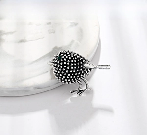 Macro detail of a vintage silver bird brooch with textured feathers and green rhinestone eye