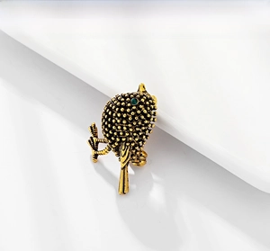 Detailed close-up of retro sparrow brooch with gold feathers and green gemstone eye