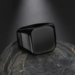 Polished black stainless steel square signet ring for men on a textured grey stone base