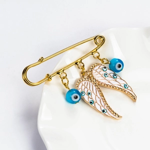 Close-up of golden angel wing brooch with blue evil eye charms on white ceramic plate