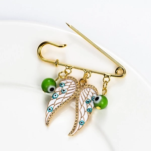 Golden angel wing brooch with evil eye beads displayed on a white ceramic plate