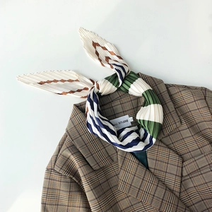 Detail of pleated striped silk scarf styled with a brown checkered blazer on white background