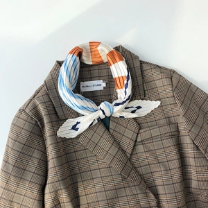 Pleated geometric striped scarf styled on a brown houndstooth blazer lapel